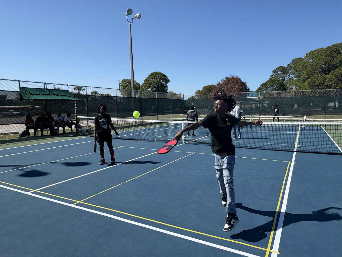 A young player leaping into a forehand as the ball hangs above the net.