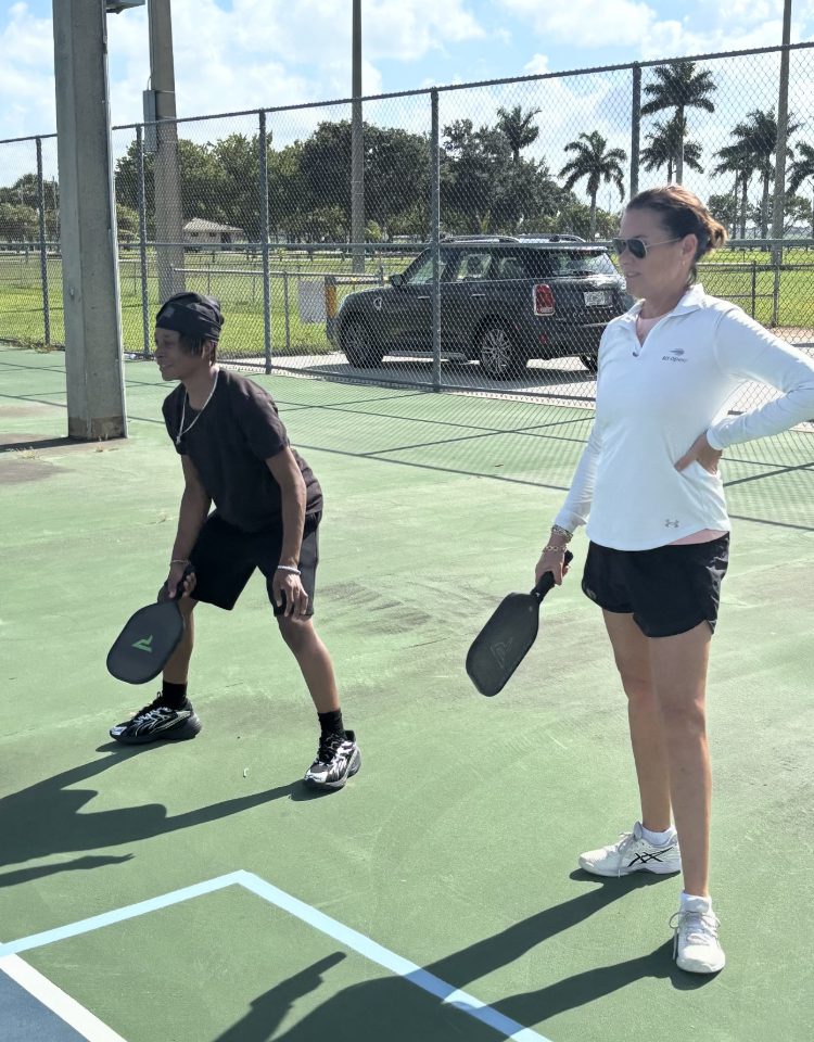 A coach and a teen player in ready position on an outdoor court.